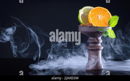 Obstschale mit Tabak, Mandarine, Limette, Minze und Rauch auf schwarzem Hintergrund Stockfoto
