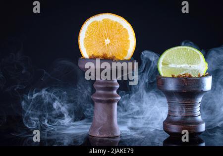Obstanhooka-Schalen mit Tabak, Limette, Orange und Rauch auf schwarzem Hintergrund Stockfoto