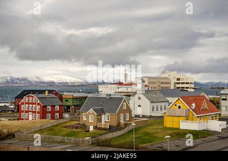 Stykkisholmur, Island, 3. Mai 2022: Bunte Häuser, eine Kirche und das Krankenhaus unter wolkendem Himmel, mit Fjord und Bergen im Hintergrund Stockfoto