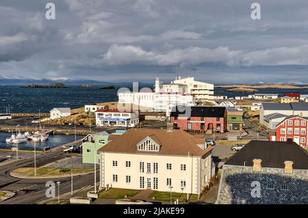Stykkisholmur, Island, 3. Mai 2022: Die Abendsonne beleuchtet Häuser, das Krankenhaus und andere Gebäude rund um den Hafen Stockfoto