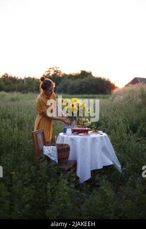 Garten und Stillleben. Teeparty im Garten - Mädchen und Strauß mit Sonnenblumen auf dem Tisch Stockfoto