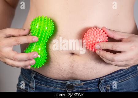 Ein Mann hält zwei Anti-Cellulite-Massagegeräte vor dem Hintergrund eines dicken Bauches. Fettverbrennung mit Verfahren. Schneller Gewichtsverlust. Stockfoto