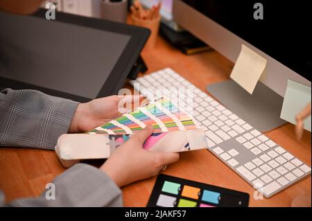 Grafikdesignerin oder Innenarchitektin prüft und wählt die Farbe aus der Farbpalette für ihr Projekt am Schreibtisch aus. cropp Stockfoto