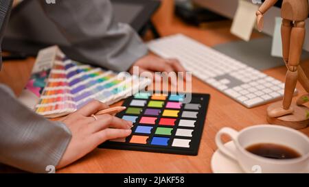 Professionelle Grafikdesignerin, die an ihrem Schreibtisch arbeitet, ihr Webdesign-Projekt plant und die Farben von Paletten und Schachbrettmuster untersucht Stockfoto