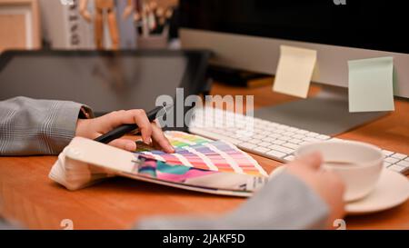 Die Innenarchitektin sitzt an ihrem Büroarbeitsplatz, schlürft Kaffee und untersucht die Farben der Farbpaletten. Stockfoto