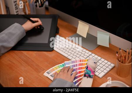 Professionelle Webgrafikerin sitzt an ihrem Schreibtisch, benutzt ein Grafiktablett, untersucht Farbmuster und arbeitet an ihrem Projekt. To Stockfoto