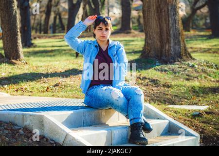 Schönes Mädchen mit kurzen schwarzen Haaren in ihrem 20s im Park trägt hellblaue Jeans und eine hellblaue Denim-Jacke Stockfoto