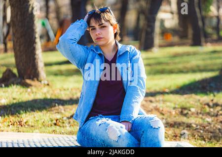 Schönes Mädchen mit kurzen schwarzen Haaren in ihrem 20s im Park trägt hellblaue Jeans und eine hellblaue Denim-Jacke Stockfoto