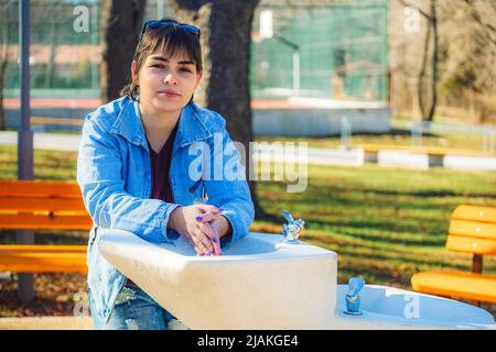 Schönes Mädchen mit kurzen schwarzen Haaren in ihrem 20s im Park trägt hellblaue Jeans und eine hellblaue Denim-Jacke Stockfoto