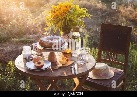 Garten und Stillleben. Teeparty im Garten - Pfirsichkuchen, Vase mit Blumenstrauß auf einem Tisch Stockfoto