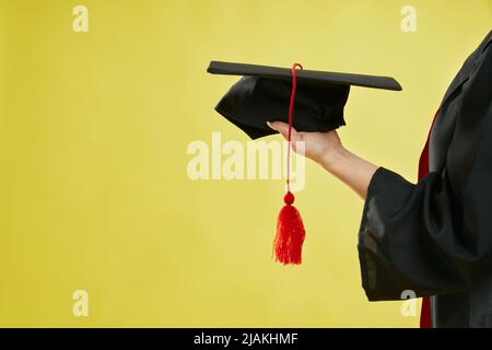 Nahaufnahme einer Studentin, die das Leichenbrett auf der Handfläche hält. Mädchen trägt Graduiertenkleid, zeigt Graduiertenmütze, Abschluss von der Hochschule. Isolieren Sie den grünen Studiohintergrund, Stockfoto