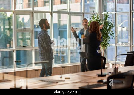 Lächelnde Gruppe junger Geschäftsleute, die sich in einem Büro unterhalten Stockfoto