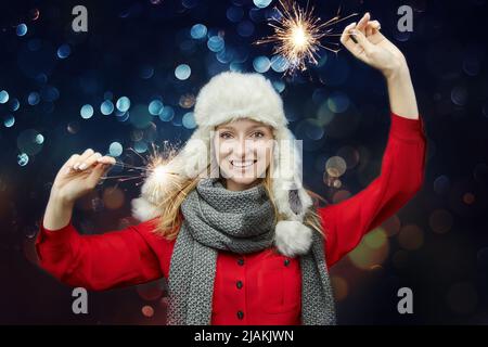 Attraktives Mädchen in einem Winterhut hält Wunderkerzen in den Händen. Stockfoto