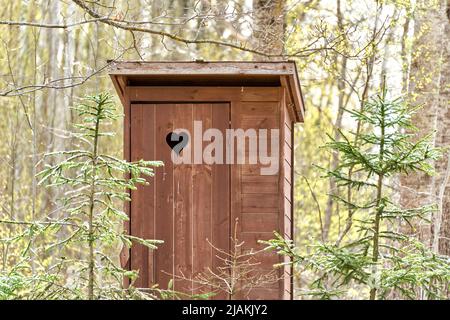 Holztoilette im Freien mit Herz an der Tür. Fichten um. Stockfoto