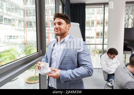 Junger Geschäftsmann, der eine Tasse Kaffee trinkt, um sich während einer Pause im Büro zu entspannen Stockfoto