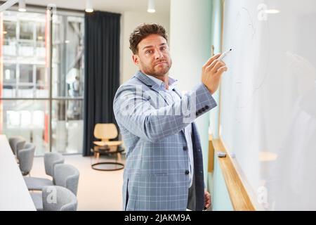 Dozent oder Unternehmensberater, der in einem Vortrag eine Präsentation auf dem Whiteboard hält Stockfoto