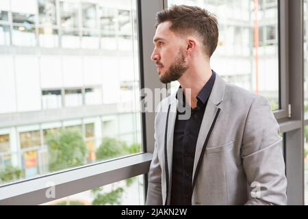 Der junge Geschäftsmann als Start-up-Gründer schaut nachdenklich aus dem Fenster im Büro Stockfoto