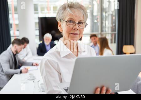 Geschäftsfrau als Geschäftsführerin mit Laptop-Computer in einem Gespräch mit dem Team im Hintergrund Stockfoto