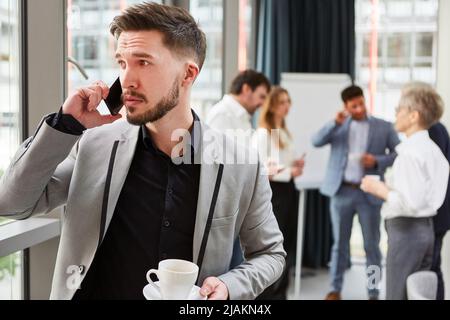 Der junge Mann als Start-up-Gründer ruft während einer Kaffeepause auf seinem Smartphone an Stockfoto