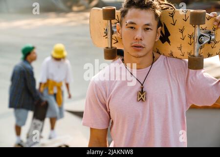 Asiatischer Junge hält Skateboard, während er Zeit im Skatepark im Freien verbringt Stockfoto