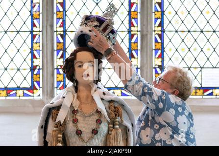 Lois Gill platziert die Krone auf einem lebensgroßen Strickmodell von Königin Elizabeth II. In ihrer örtlichen Kirche in Caston bei Norwich, Norfolk, wo sie während der Feierlichkeiten zum Platin-Jubiläum ausgestellt wird. Die Wollkreation wurde ursprünglich von Frau Gill, Penny Evans und einer lokalen Gruppe von Strickern für den 65.. Jahrestag der Krönung der Königin im Jahr 2017 hergestellt und dauerte 6 Monate, bis sie mit über 1000 Wollbällen beendet wurde. Bilddatum: Dienstag, 31. Mai 2022. Stockfoto