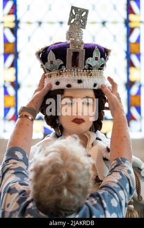 Lois Gill platziert die Krone auf einem lebensgroßen Strickmodell von Königin Elizabeth II. In ihrer örtlichen Kirche in Caston bei Norwich, Norfolk, wo sie während der Feierlichkeiten zum Platin-Jubiläum ausgestellt wird. Die Wollkreation wurde ursprünglich von Frau Gill, Penny Evans und einer lokalen Gruppe von Strickern für den 65.. Jahrestag der Krönung der Königin im Jahr 2017 hergestellt und dauerte 6 Monate, bis sie mit über 1000 Wollbällen beendet wurde. Bilddatum: Dienstag, 31. Mai 2022. Stockfoto