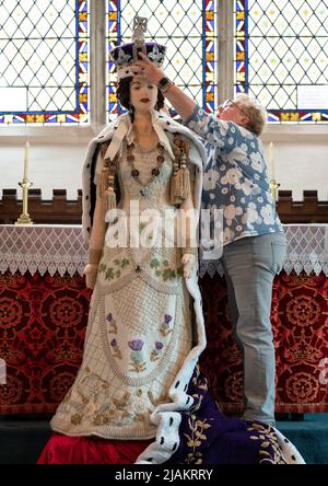 Lois Gill platziert die Krone auf einem lebensgroßen Strickmodell von Königin Elizabeth II. In ihrer örtlichen Kirche in Caston bei Norwich, Norfolk, wo sie während der Feierlichkeiten zum Platin-Jubiläum ausgestellt wird. Die Wollkreation wurde ursprünglich von Frau Gill, Penny Evans und einer lokalen Gruppe von Strickern für den 65.. Jahrestag der Krönung der Königin im Jahr 2017 hergestellt und dauerte 6 Monate, bis sie mit über 1000 Wollbällen beendet wurde. Bilddatum: Dienstag, 31. Mai 2022. Stockfoto