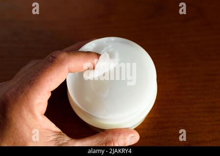 Ein Mann nimmt weiße Vaseline auf, um seine Haut mit dunklem Hintergrund zu befeuchten. Stockfoto