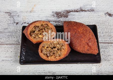 Kibbeh auf weißem Holzhintergrund. Kibbeh ist ein beliebtes Gericht in der nahöstlichen Küche. Gefüllte Fleischbällchen Essen, Falafel, icli Kofta, Quibe. Draufsicht. E Stockfoto