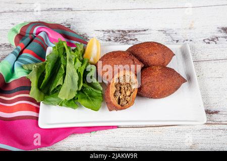 Kibbeh auf weißem Holzhintergrund. Kibbeh ist ein beliebtes Gericht in der nahöstlichen Küche. Gefüllte Fleischbällchen Essen, Falafel, icli Kofta, Quibe. Draufsicht. E Stockfoto