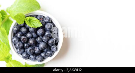 Weiße Schale mit Waldbluebeeren und frischen grünen Minzblättern auf weißem Hintergrund. Heidelbeere - natürliches Superfood. Gesunde Ernährung. Werbebanner. V Stockfoto