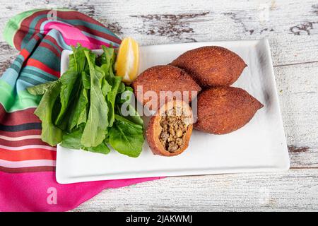 Kibbeh auf weißem Holzhintergrund. Kibbeh ist ein beliebtes Gericht in der nahöstlichen Küche. Gefüllte Fleischbällchen Essen, Falafel, icli Kofta, Quibe. Draufsicht. E Stockfoto