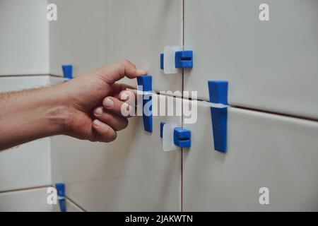 Fliesenleger mit Fliesen Nivelliersystem beim Verlegen von Keramikfliesen an der Badezimmerwand Stockfoto