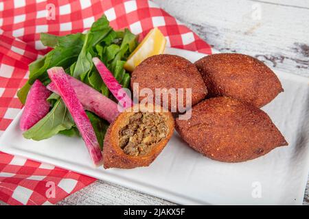 Kibbeh auf weißem Holzhintergrund. Kibbeh ist ein beliebtes Gericht in der nahöstlichen Küche. Gefüllte Fleischbällchen Essen, Falafel, icli Kofta, Quibe. Draufsicht. E Stockfoto