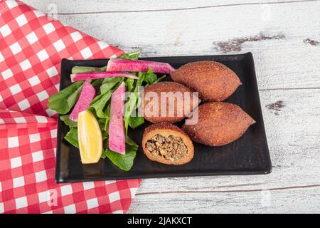 Kibbeh auf weißem Holzhintergrund. Kibbeh ist ein beliebtes Gericht in der nahöstlichen Küche. Gefüllte Fleischbällchen Essen, Falafel, icli Kofta, Quibe. Draufsicht. E Stockfoto