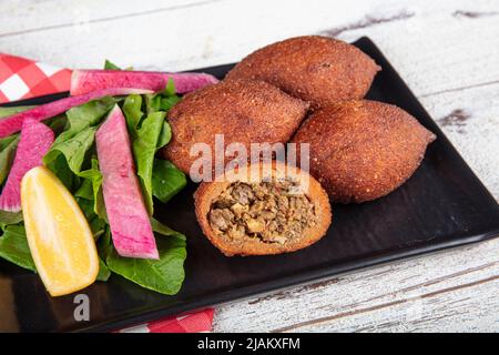 Kibbeh auf weißem Holzhintergrund. Kibbeh ist ein beliebtes Gericht in der nahöstlichen Küche. Gefüllte Fleischbällchen Essen, Falafel, icli Kofta, Quibe. Draufsicht. E Stockfoto