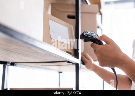 Beschnittene Ansicht des afroamerikanischen Verkäufers, der Versandetikett auf der Verpackung im Geschäft scannt Stockfoto