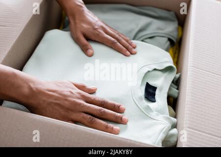 Beschnittene Ansicht der afroamerikanischen Verkäufer Putting Kleidung in Paket im Online-Shop Stockfoto