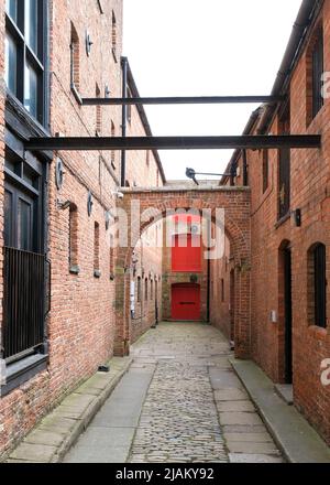 Hull, East Yorkshire, Großbritannien. 21. Mai 2022 Eine gepflasterte Straße in der Altstadt mit einem eleganten Torbogen, alten Stahlträgern, Bindebögen und roten Türen Stockfoto