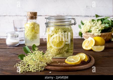 Holunderbeerenwasser oder Sirup mit frischen Blumen und Zitronen, Zucker. Holzhintergrund Stockfoto