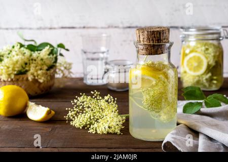 Holunderbeerenwasser oder Sirup aus frischen Blumen, Zitronen, Zucker. Weißer und brauner Holzhintergrund Stockfoto