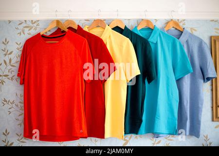 In einem Schlafzimmer hängt eine bunte Reihe frisch gewaschenen Herren-T-Shirts/Poloshirts an einer Bildschiene. Stockfoto