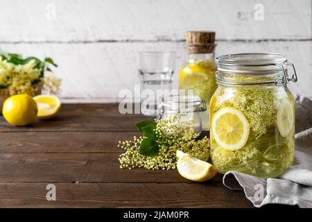 Holunderwasser oder Sirup mit frischen Blumen und Zitronen. Speicherplatz kopieren. Holzhintergrund Stockfoto