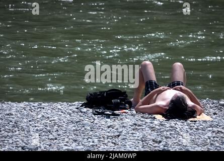 München, Deutschland. 31.. Mai 2022. Ein Mann liegt in der Sonne auf einem Kiesufer an der Isar. Quelle: Jann Philip Gronenberg/dpa/Alamy Live News Stockfoto