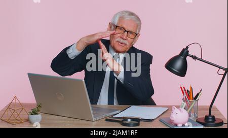 Müde ernsthafte verärgert Senior Geschäftsmann zeigt Auszeit Geste, Grenze oder Stopp-Zeichen, kein Druck, ich brauche mehr Zeit sitzt am Arbeitsplatz Schreibtisch im Büro. Älterer Mann isoliert auf rosa Studio Wand Hintergrund Stockfoto