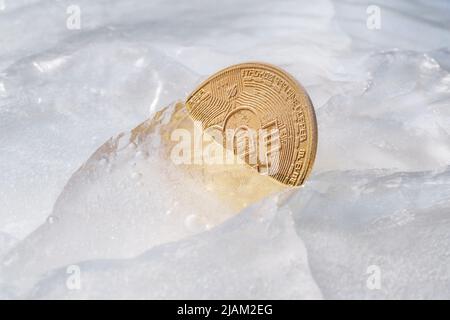Goldene Münze mit Bitcoin-Symbol, eingefroren in Eis. Einfrieren von Kryptowährung, Abschreibungen, rechtliche und wirtschaftliche Probleme des Kryptowährungsmarktes sie Stockfoto