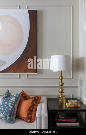 Beistelltisch mit Messinglampe, modernen Kunstwerken und getäfelten Wänden Stockfoto
