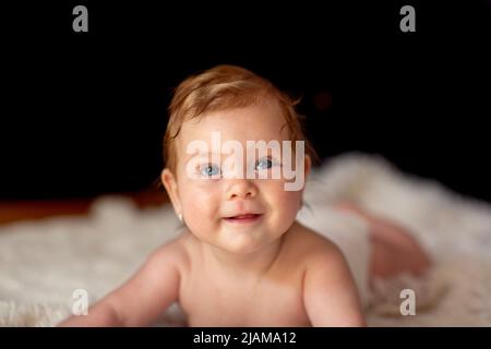 Schöne blaue Augen.lächelndes Baby Mädchen auf ihrem Bauch genießt und kriecht Stockfoto