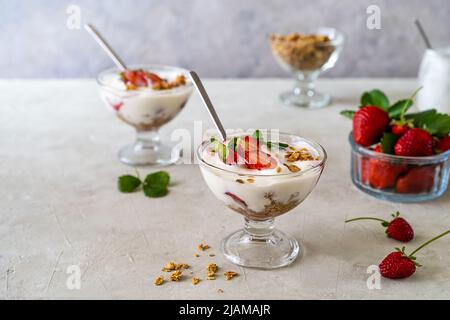 Joghurt mit Erdbeerkompott und Müsli, mit frischen Früchten in Dessertbechern auf grauem Hintergrund. Speicherplatz kopieren Stockfoto