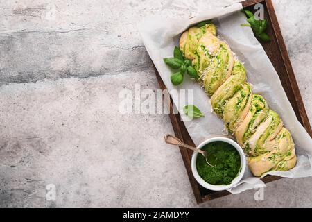 Geflochtenes Bärlauch-Pesto Brioche. Hausgemachtes rohes oder ungekochte frisches Pull-Apart-Brot mit Bärlauch-Pesto auf Holzbrett auf altem grauen Hintergrundtisch Stockfoto